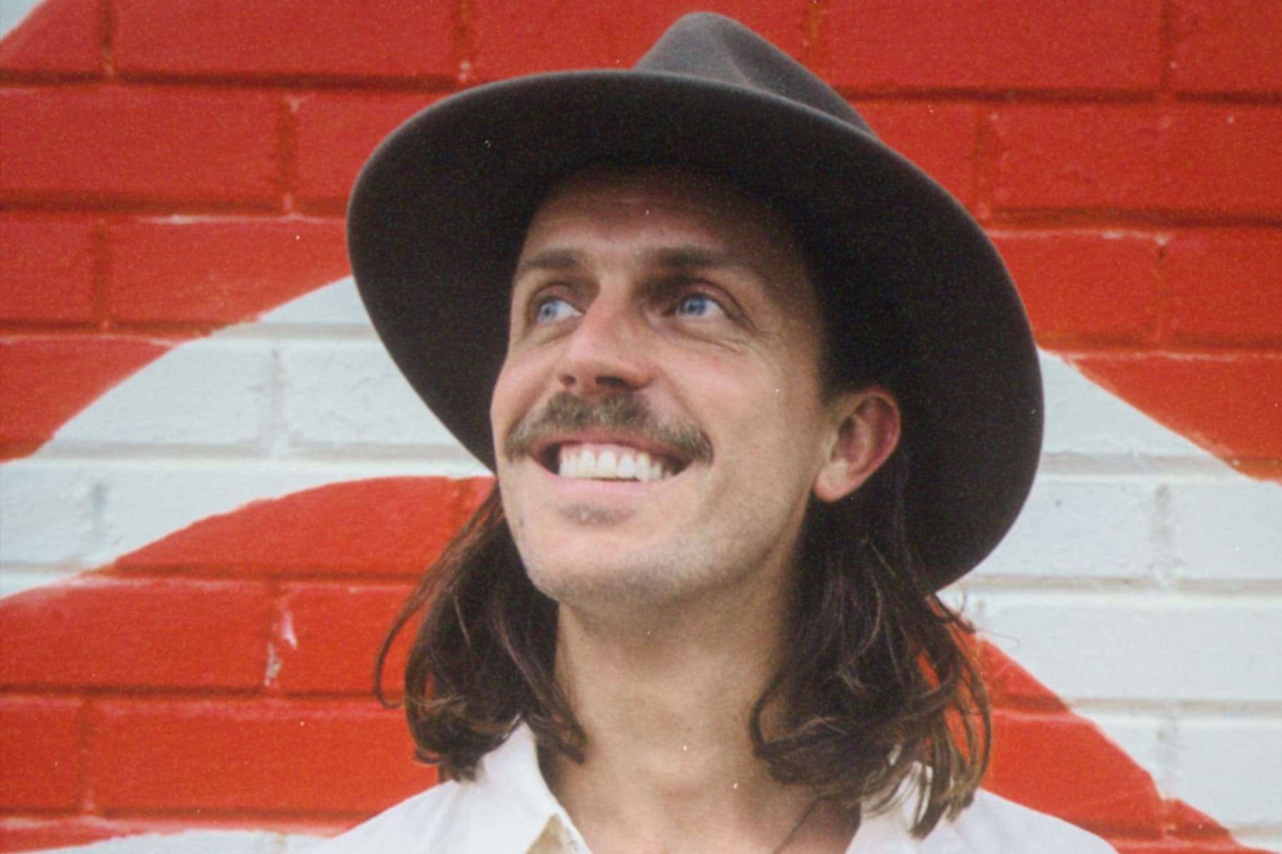 Benjo smiling in a hat against red and white stripes